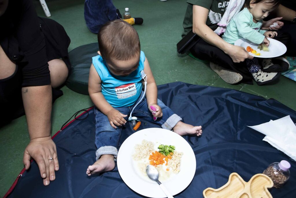 Bebê sentado no tapete explorando um prato de comida na introdução alimentar