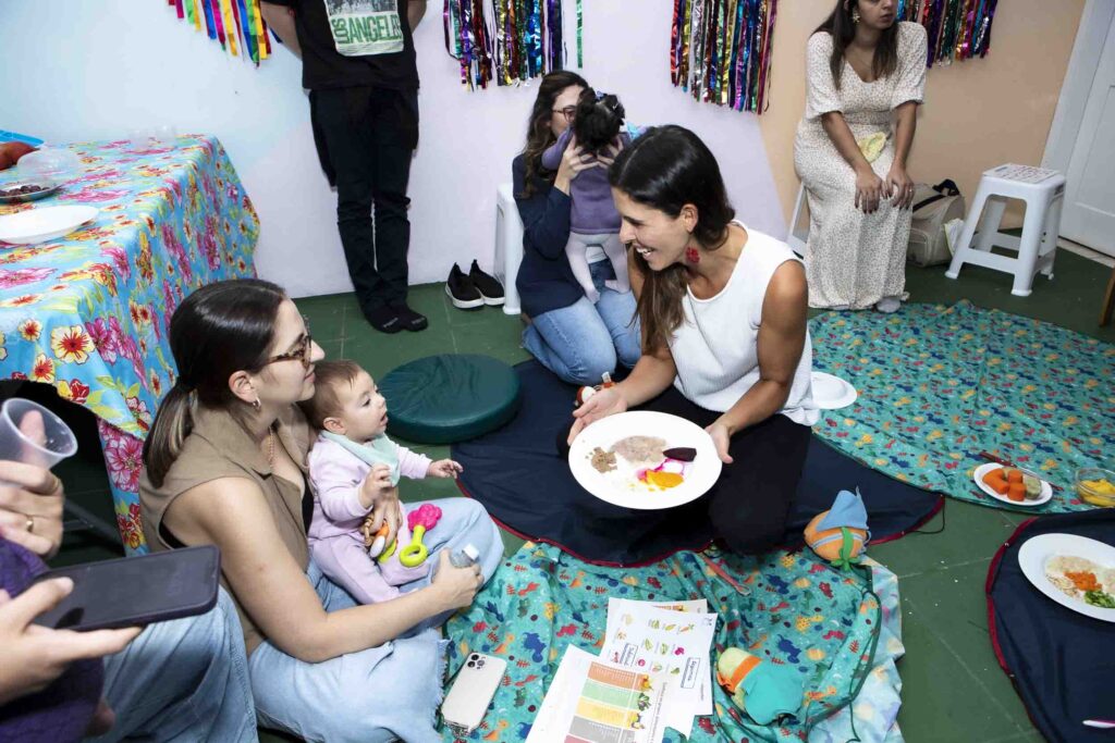 Nutricionista Priscila Guedes mostrando um prato de introdução alimentar para uma mãe e seu bebê
