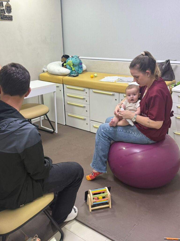 Fisioterapeuta pediátrica Stephanie com bebê na bola suíça durante sessão de fisioterapia