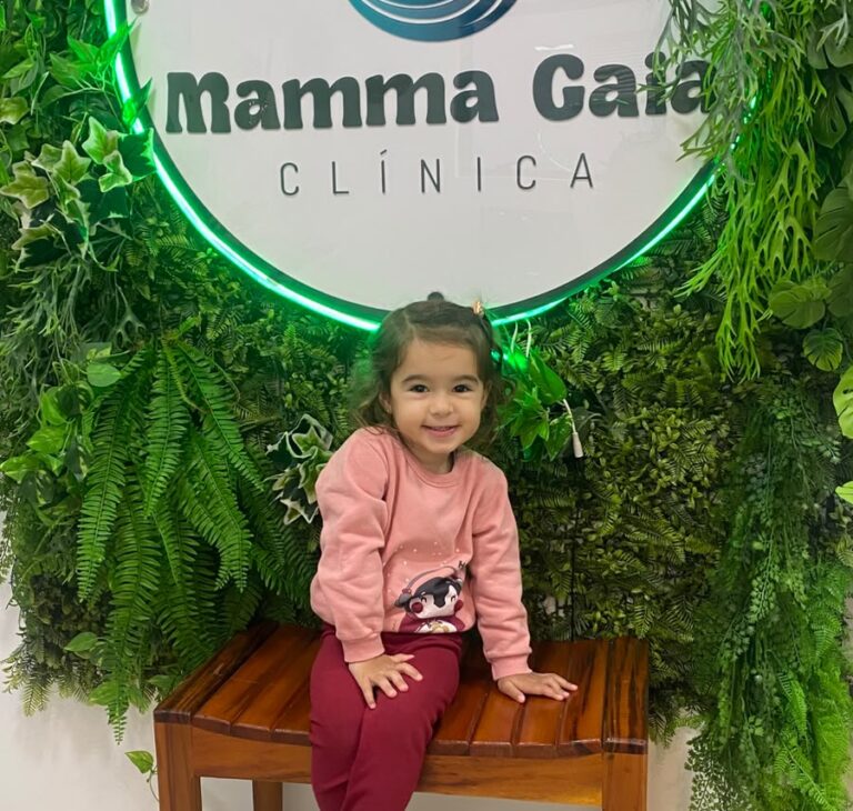 Criança sorrindo em frente ao painel verde da recepção da Clínica Mamma Gaia