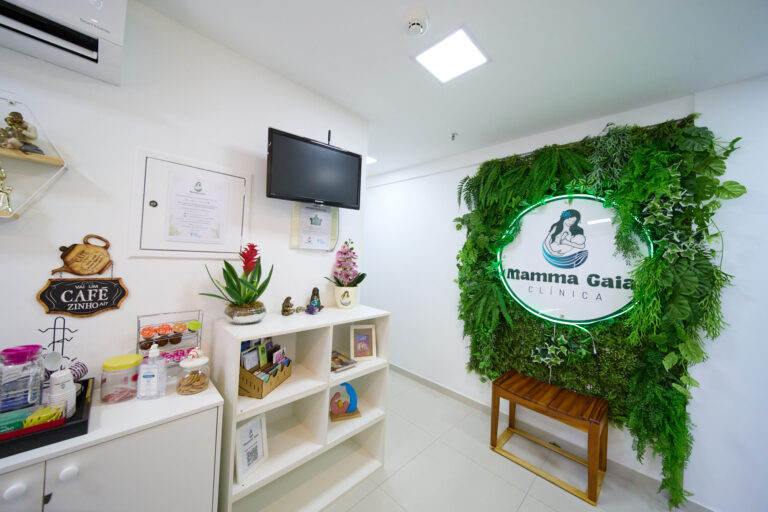 Recepção da Clínica Mamma Gaia com café e painel de plantas com o logo