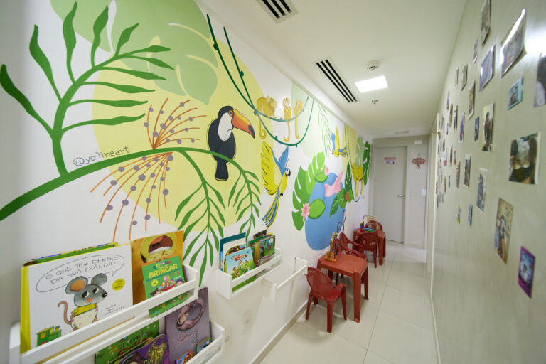 Corredor da Clínica Mamma Gaia com mural de natureza, livros e mesinhas infantis