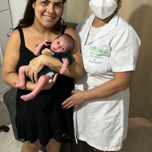 Consultora Milene segurando recém-nascido ao lado da mãe durante consultoria